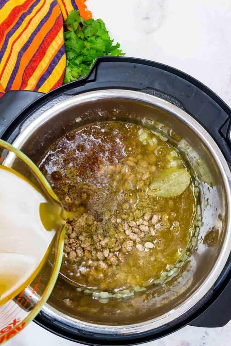 Broth poured overtop pinto beans and seasonings in the instant pot.