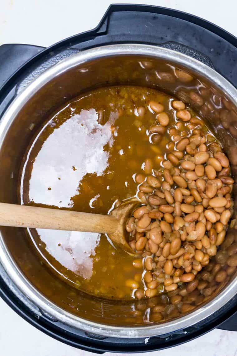 A wooden spoon stirs cooked pinto beans inside the instant pot.