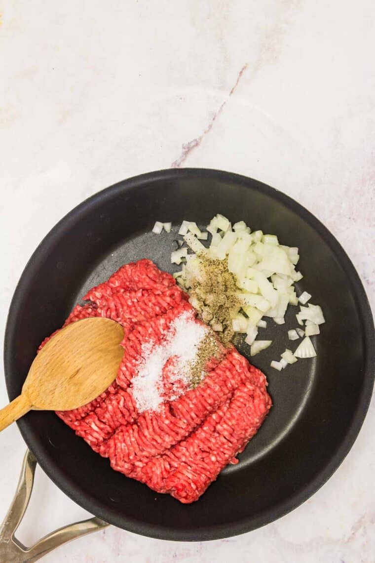 Onions, garlic, and seasonings combined in a skillet with a wooden spoon.