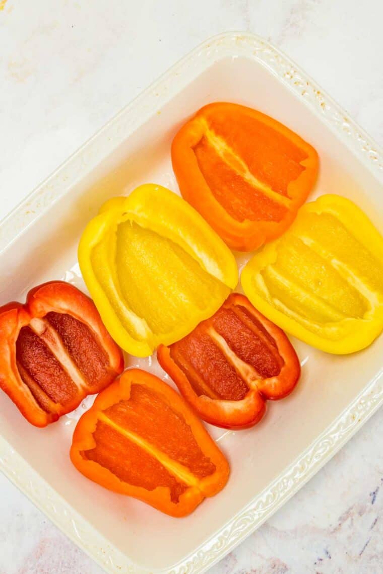 Red, yellow, and orange bell pepper halves arranged in a white ceramic baking dish.
