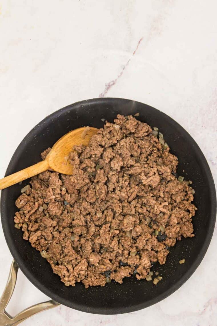 Browned ground beef in a skillet with a wooden spoon.