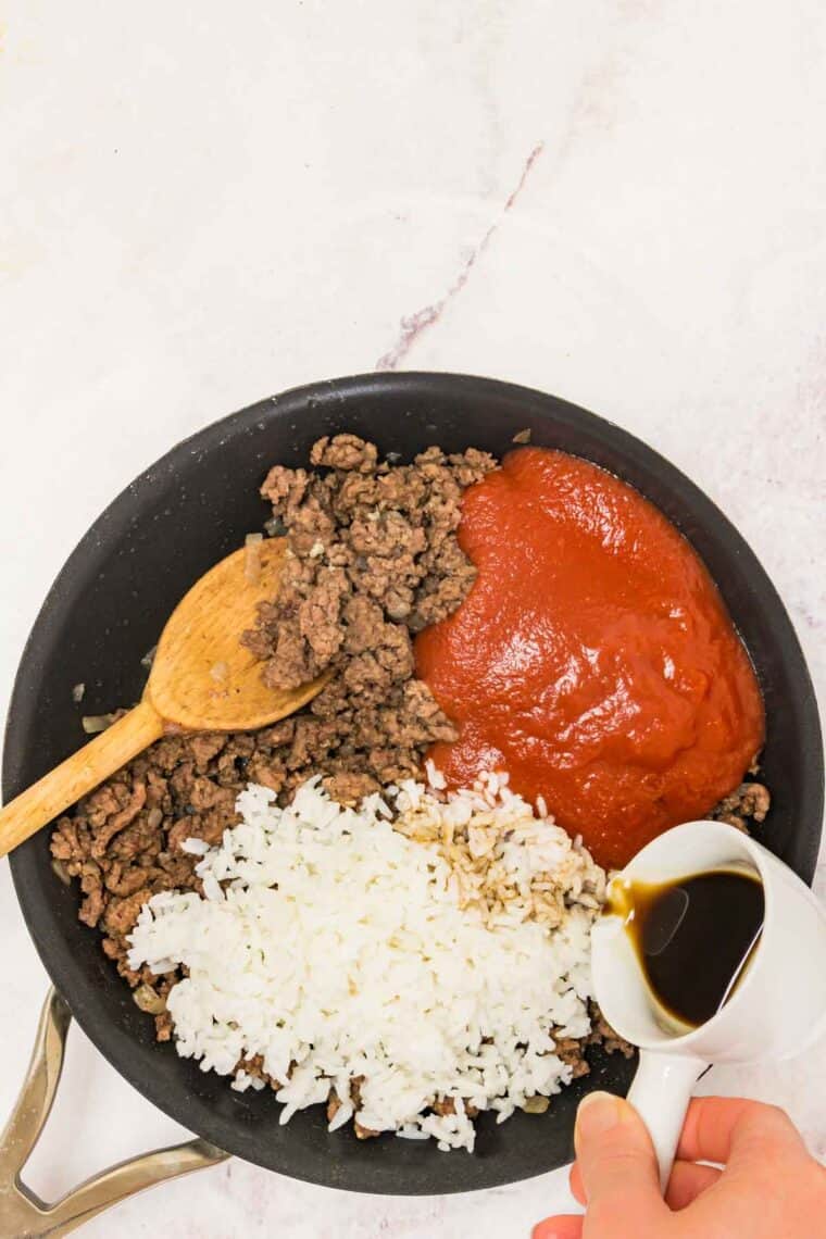 Worcestershire sauce is poured into a skillet with rice, tomato sauce, and cooked ground beef.