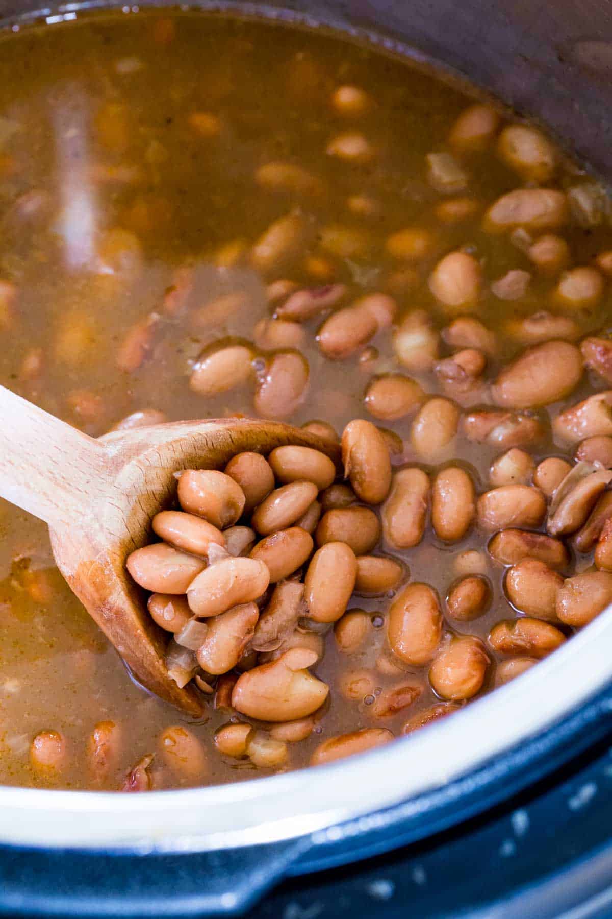 A wooden spoon stirs pinto beans with broth inside the instant pot.