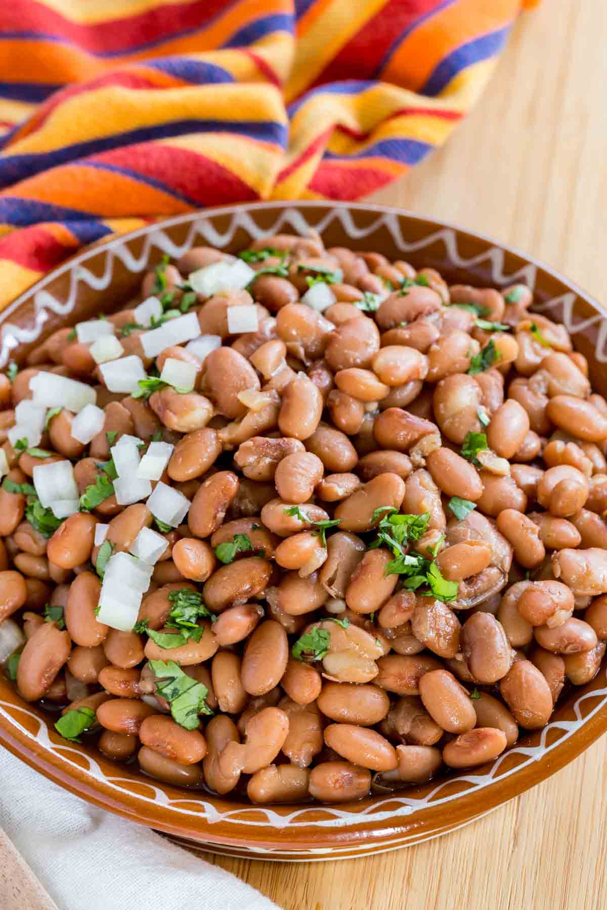 Instant Pot pinto beans in a large brown bowl, garnished with cilantro and diced onions.