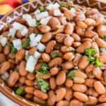 Instant Pot pinto beans in a large brown bowl, garnished with cilantro and diced onions.