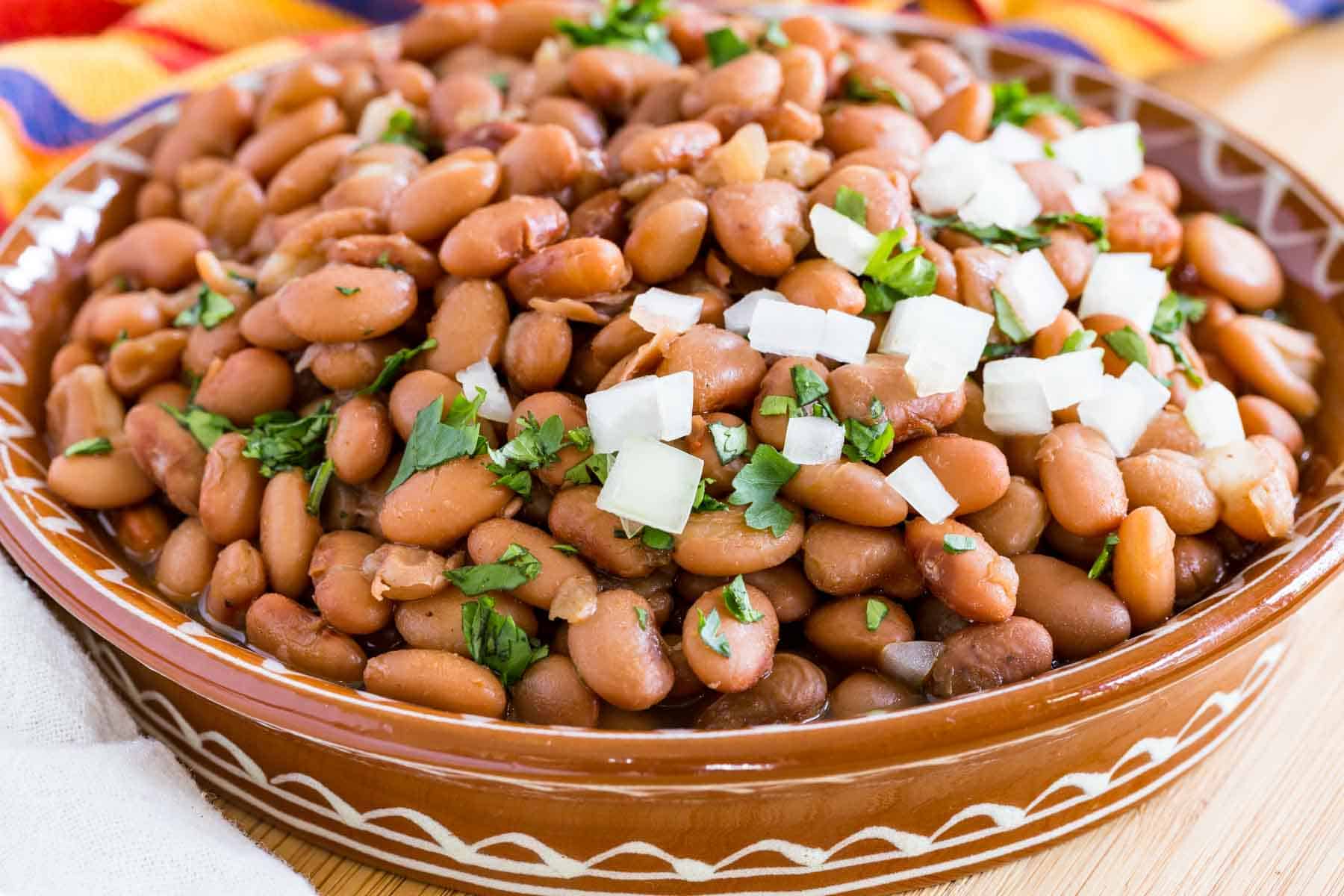 Instant Pot pinto beans in a large brown bowl, garnished with cilantro and diced onions.