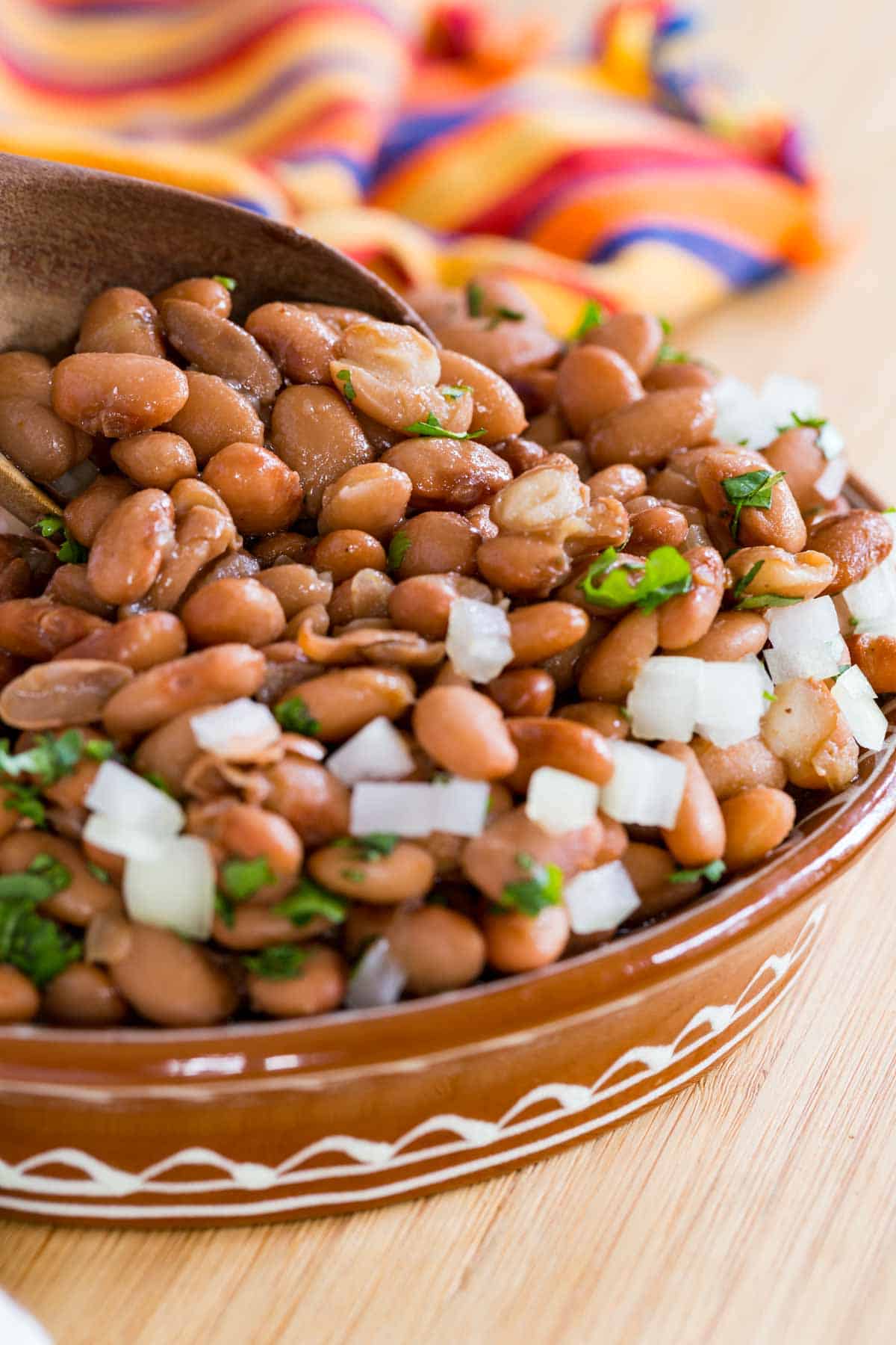 Instant Pot pinto beans in a large brown bowl, garnished with cilantro and diced onions.