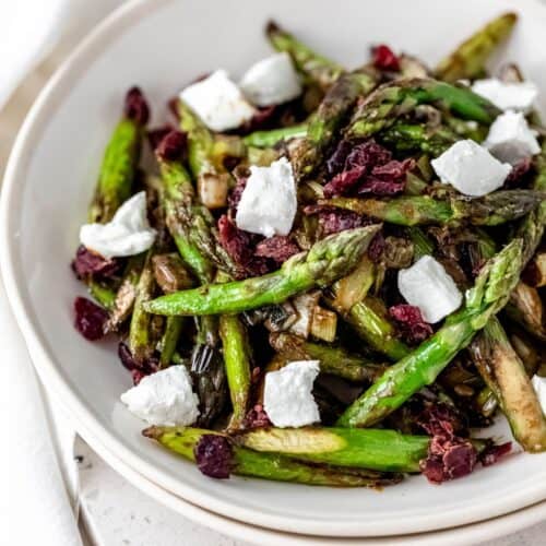 Closeup of a bowl of roasted asparagus salad with caramelized leeks, goat cheese, and dried cherries.