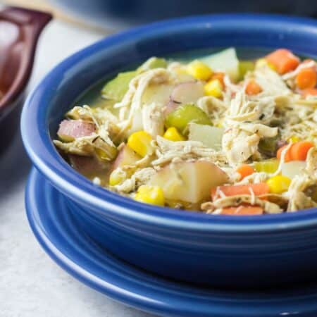 Chicken and vegetable soup in a blue bowl on top of a blue plate.