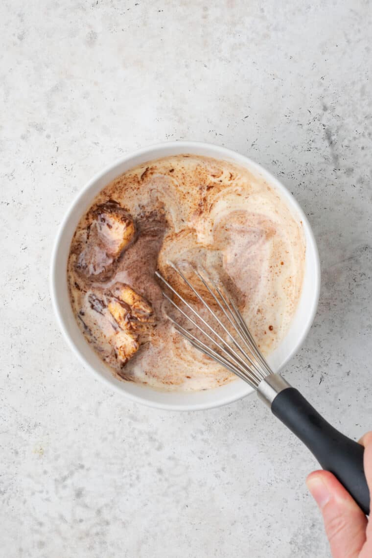 Melted chocolate whisked together with the ingredients for chocolate glaze in a bowl.