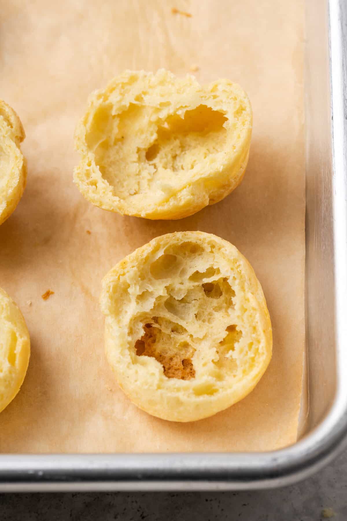 Two halves of a gluten-free cream puff on a parchment-lined baking sheet.