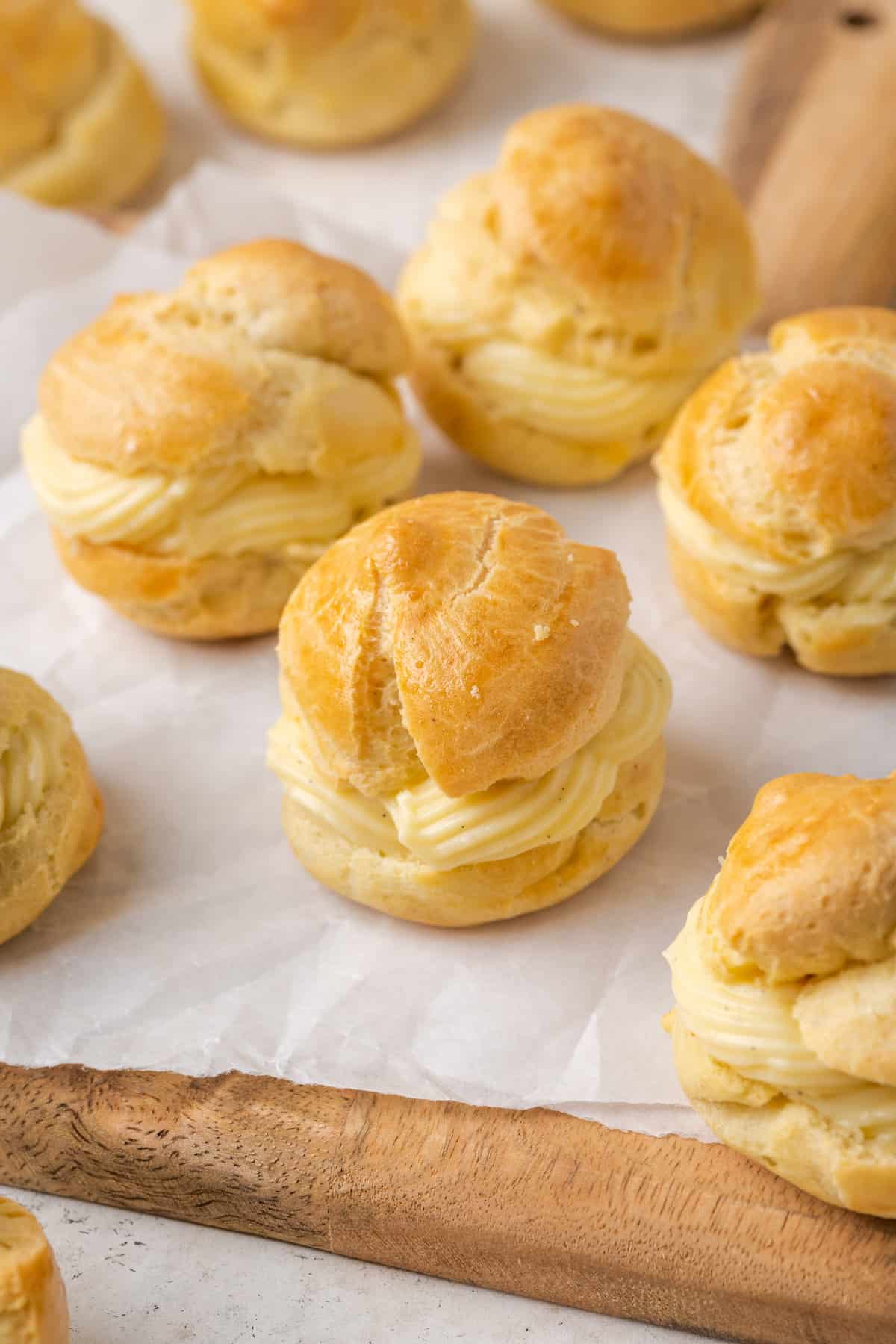 Assorted gluten-free cream puffs filled with vanilla pastry cream on a parchment-lined wooden board.