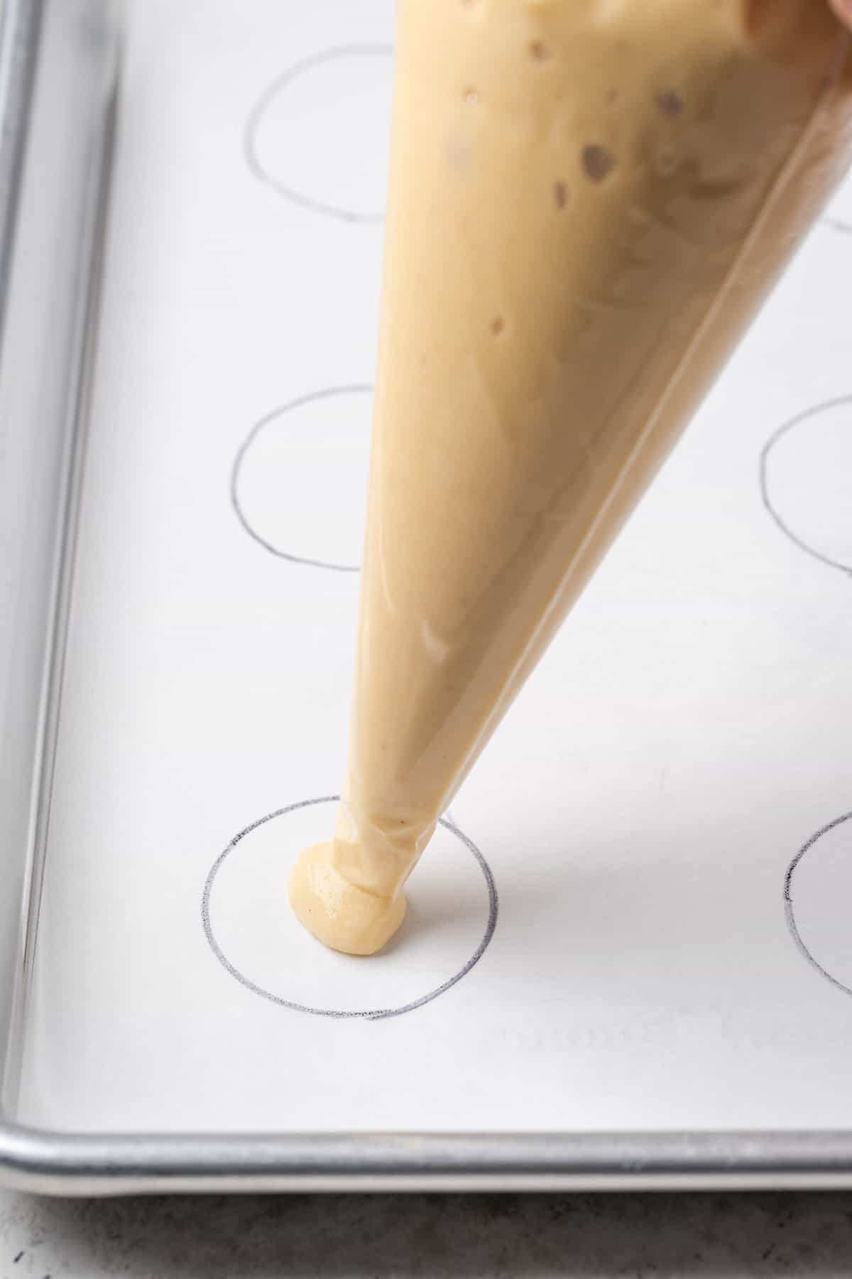 A piping bag pipes gluten-free pate a choux paste into a circle on a parchment-lined baking sheet.