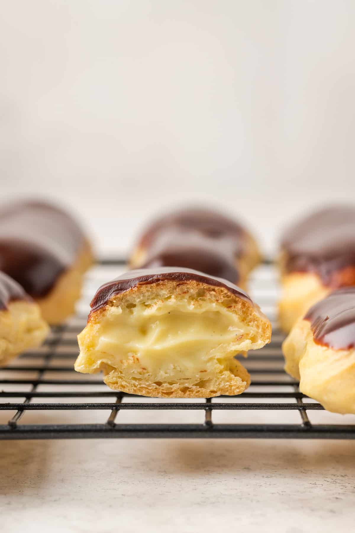 Side view of chocolate gluten-free eclairs on a wire rack, with a bite missing from the middle eclair.