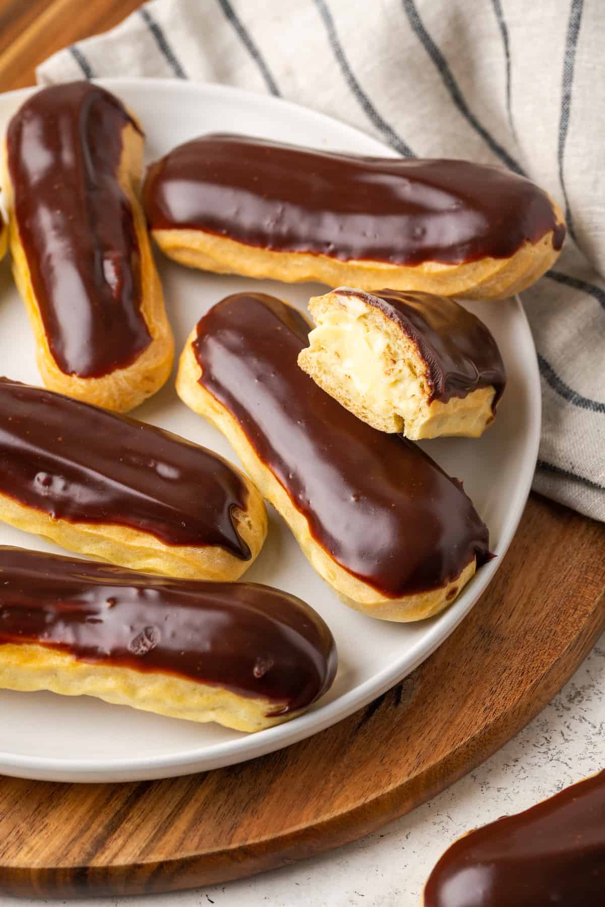 Assorted gluten-free eclairs on a white plate, with a bite missing from one.