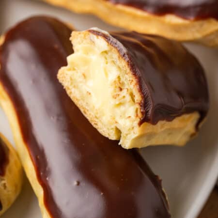 Close up of gluten-free eclairs on a white plate, with a bite missing from one.