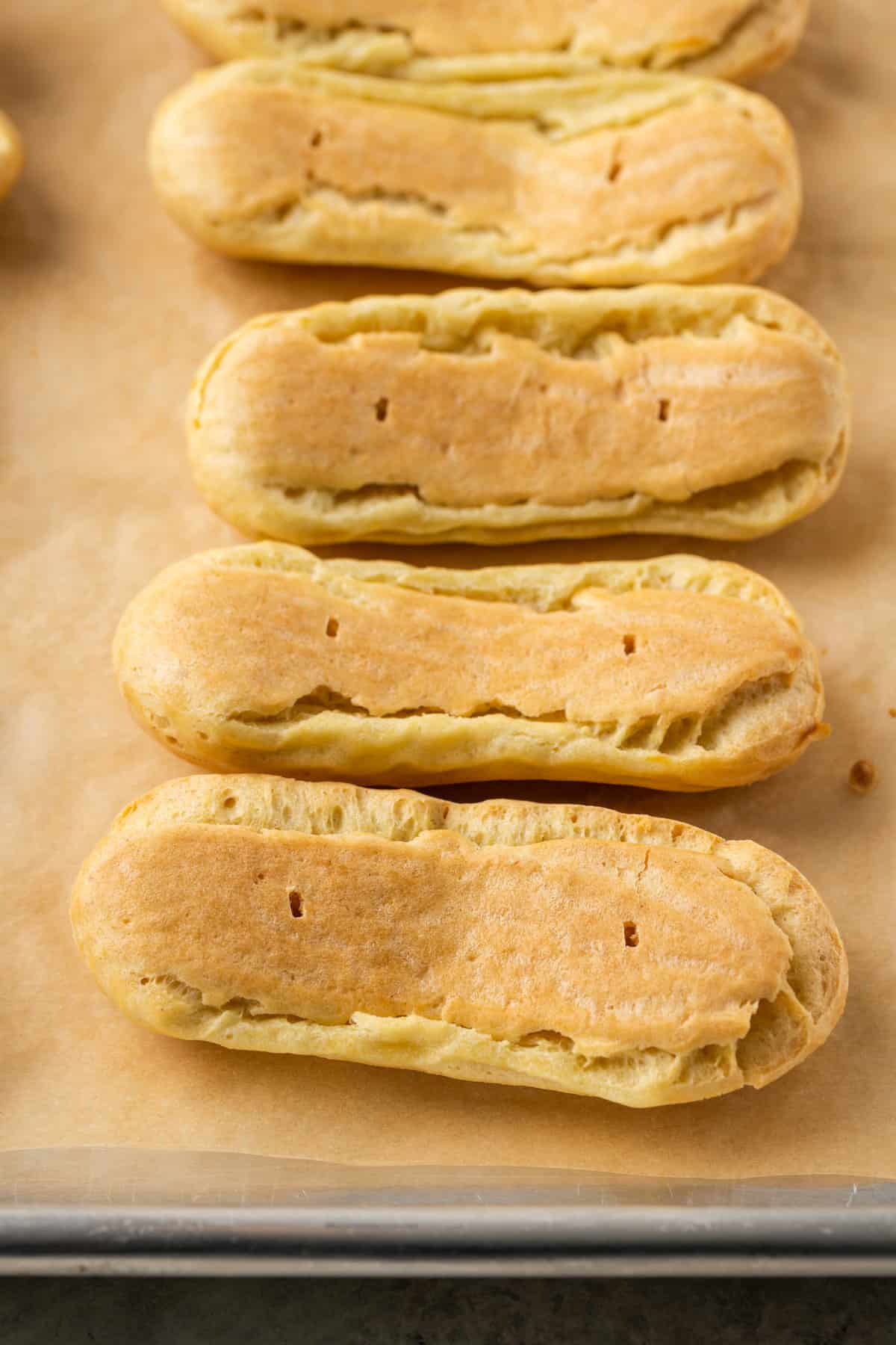 A row of gluten-free eclair pastries flipped upside down on a baking sheet lined with parchment paper.