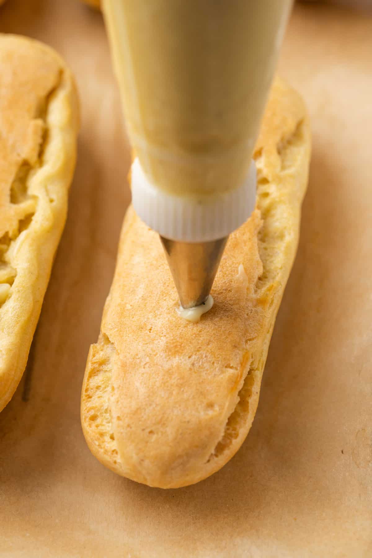A narrow piping tip pipes vanilla pastry cream into an upside-down gluten-free eclair pastry.