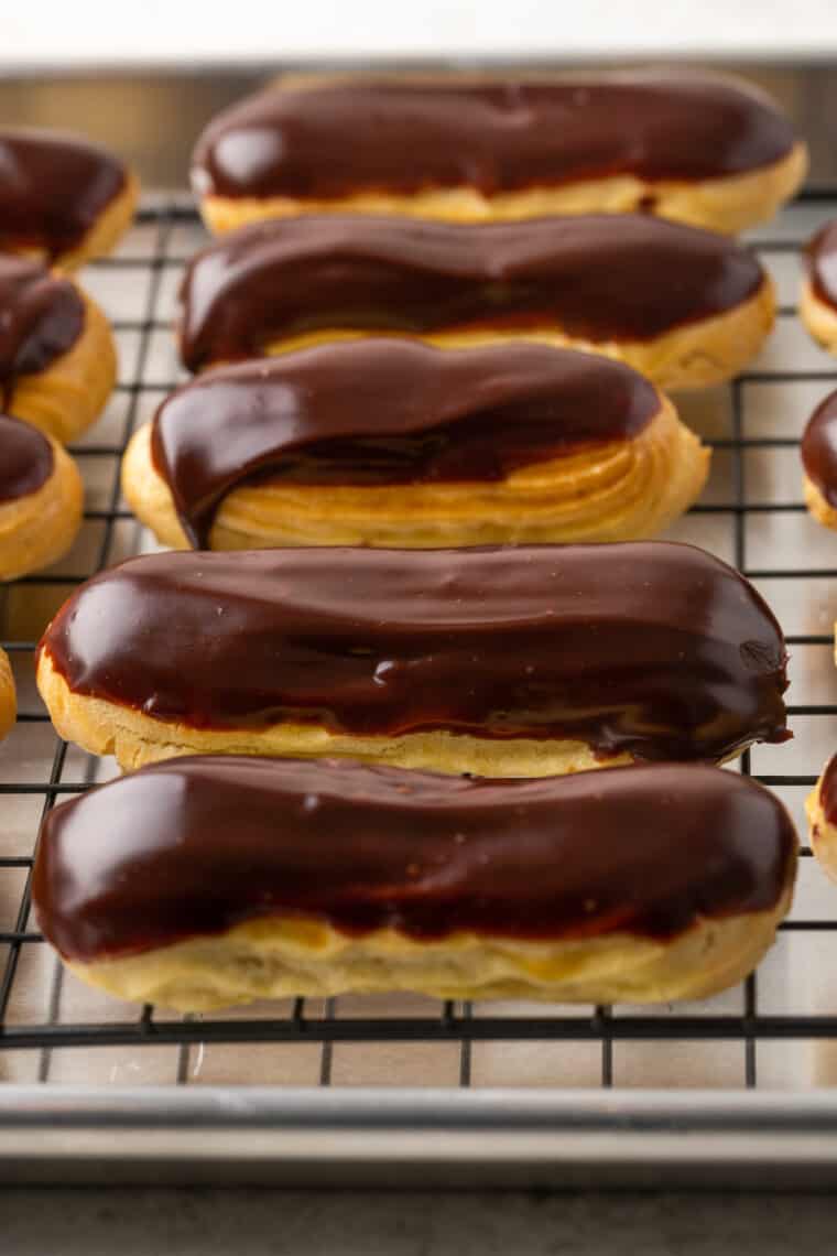 A row of chocolate dipped gluten-free eclairs on a wire rack.