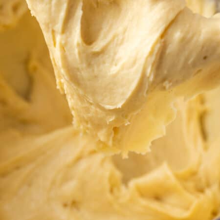 Close up of gluten free pate a choux dough stuck to a stand mixer attachment above a mixing bowl.