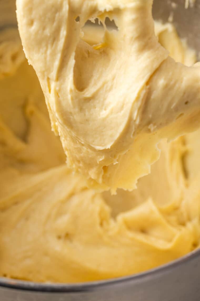 Close up of gluten free pate a choux dough stuck to a stand mixer attachment above a mixing bowl.