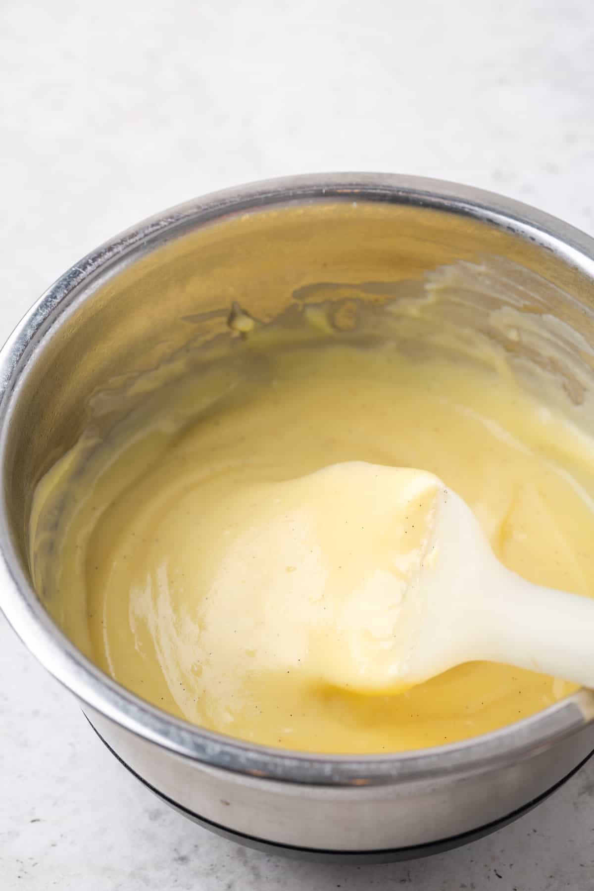 A rubber spatula stirring vanilla pastry cream in a saucepan.