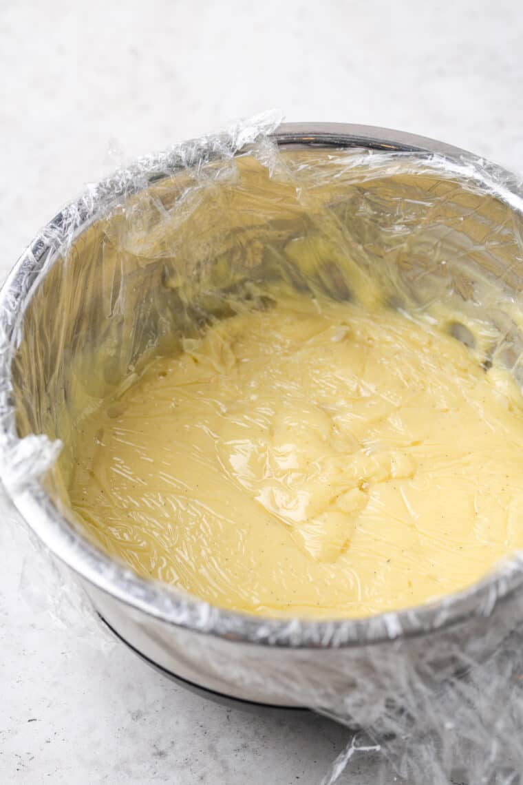 Vanilla pastry cream in a metal bowl wrapped in plastic wrap.