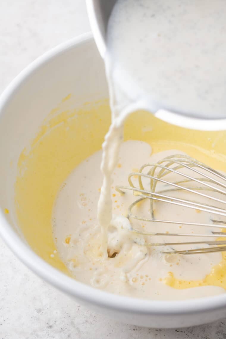 Hot milk is poured and whisked into a bowl of egg yolks.