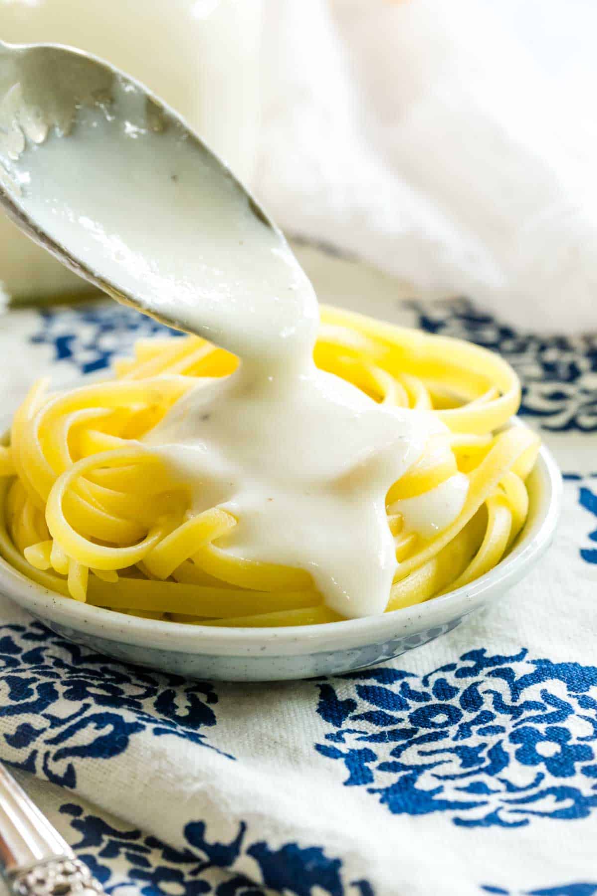 Homemade alfredo sauce is added to fettuccine with a spoon.