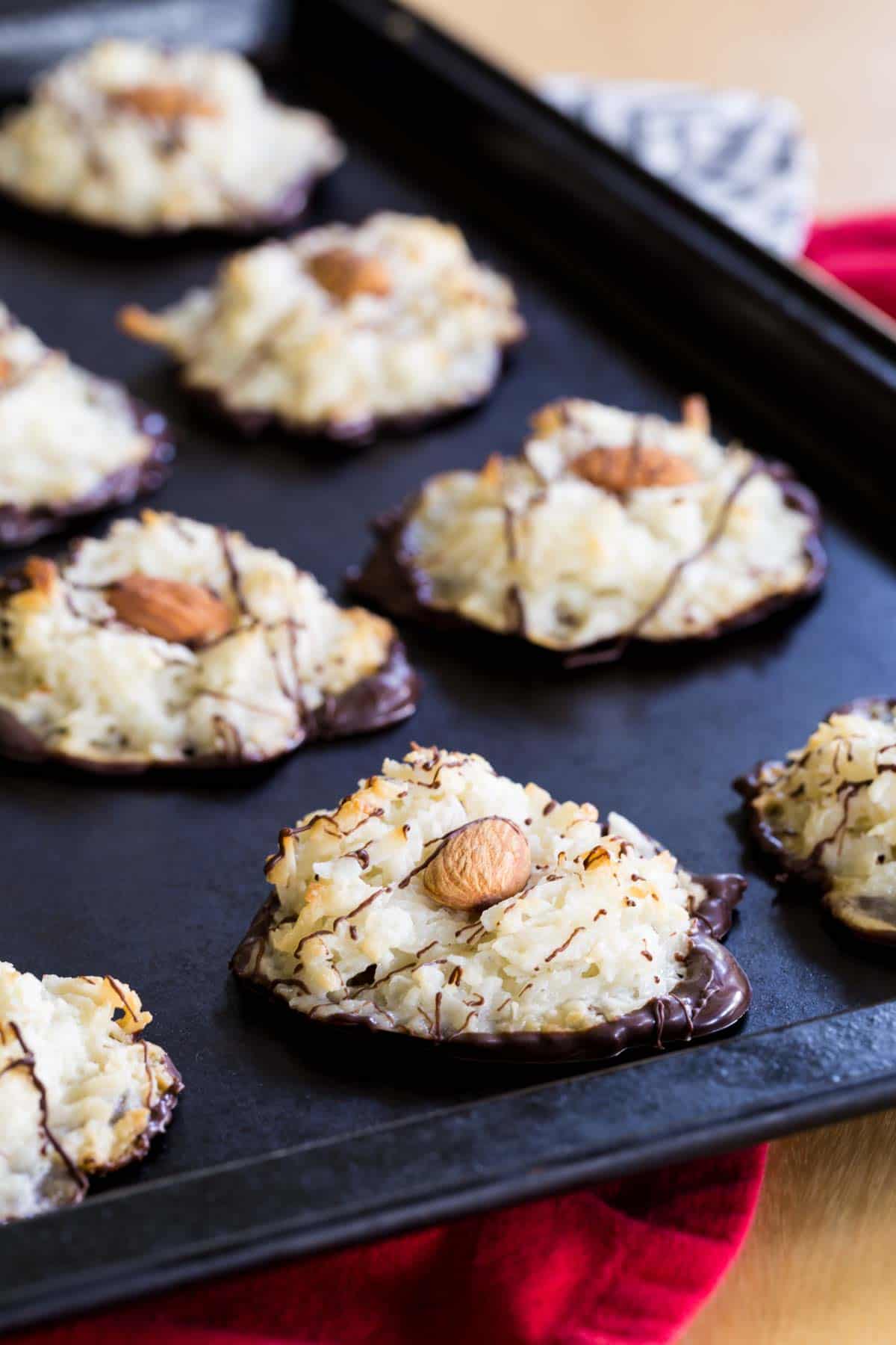 Almond Joy Cookies drizzled with chocolate on a cookie sheet resting on top of a red cloth napkin.