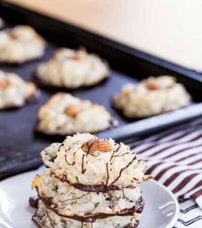 A stack of three Almond Joy Macaroons on a small white sitting on red, white, and black cloth napkins with more cookies on the sheet pan behind it.
