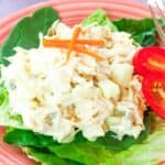 Chicken salad served over lettuce on a pink plate with text overlay that says "Apple Chicken Salad".