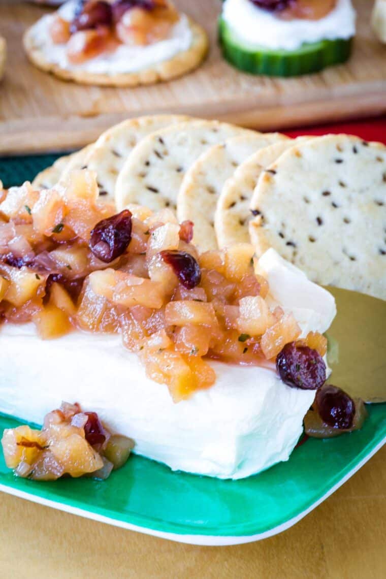 A block of cream cheese topped with apple chutney on a green plate with crackers.