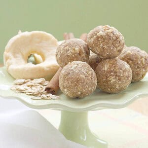 Apple energy balls on a small green stand with dried apples, cinnamon sticks, and oats.