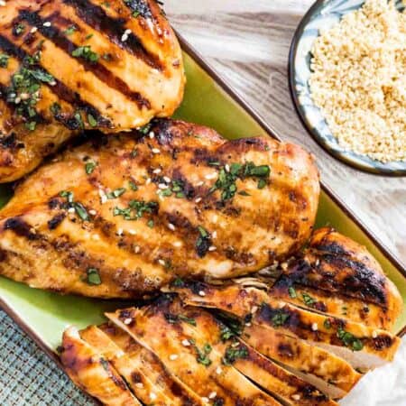 Overhead view of Asian grilled chicken breasts on a rectangular plate garnished with chopped cilantro and sesame seeds.