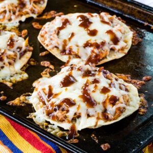 BBQ Chicken Tostadas covered with melted cheese on a sheet pan with some of the pieces of cheese melted and browned.