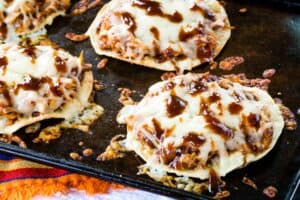 Chicken tostadas covered with melted cheese and barbecue sauce on a sheet pan.