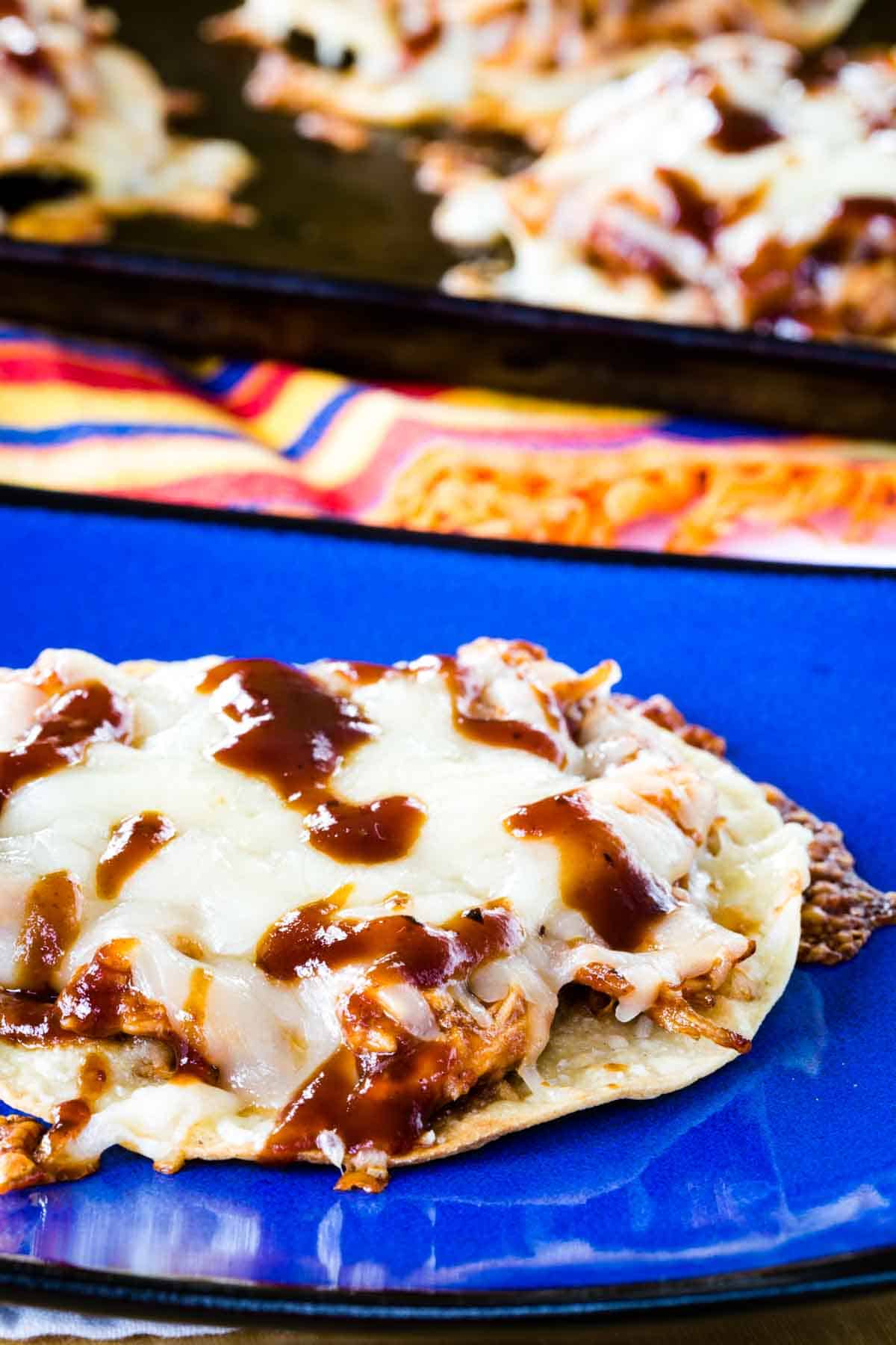A chicken tostada with barbecue sauce and cheese on a blue plate.