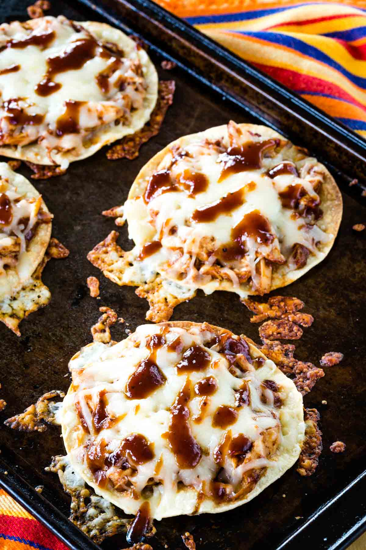 Four BBQ Chicken Tostadas drizzled with barbecue sauce on a baking sheet.