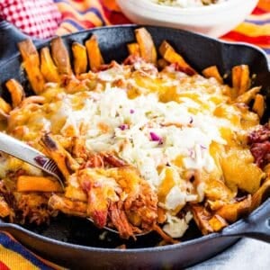 A serving spoon scooping some BBQ pulled pork fries from a skillet.
