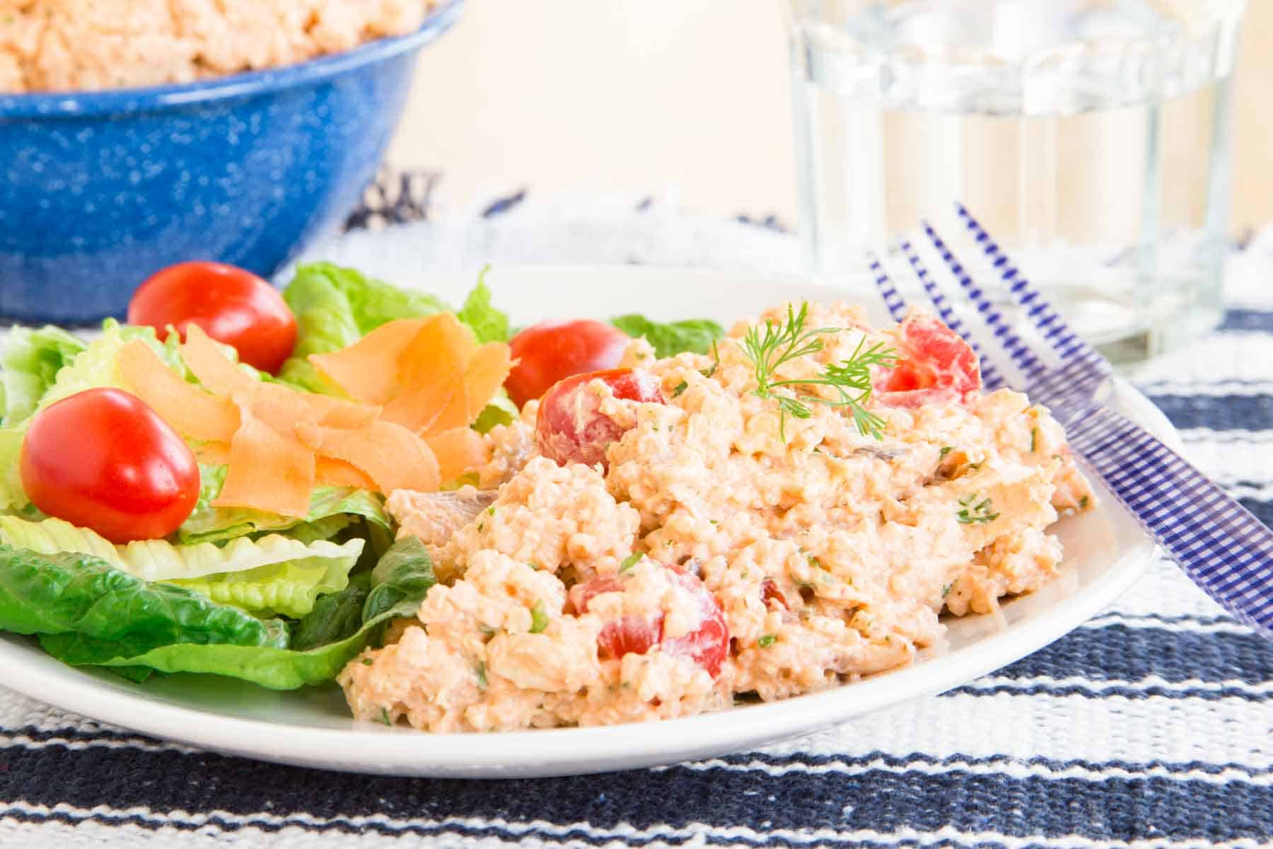 Barbecue ranch quinoa chicken salad served alongside a side green on a white plate with a fork resting on it.