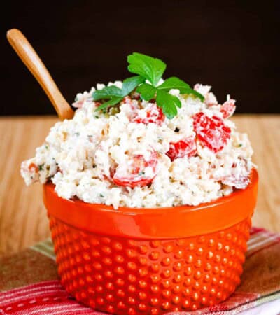 An orange bowl full of bacon ranch quinoa chicken salad with leaves of parsley on top.