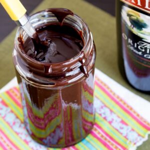 Looking down into a jar of chocolate sauce with a spoon in it and a bottle of Bailey's Irish Cream off to the side.