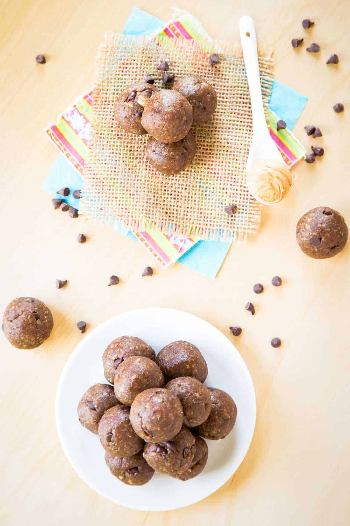 A birds eye view of a plate of energy bites with more stacked on napkins with a spoonful of peanut butter next to it.