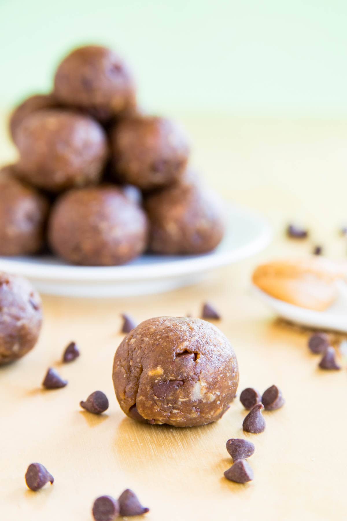 A chocolate chip peanut butter energy ball with more piled on a plate in the background.