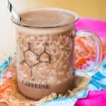 A chocolaty smoothie in a glass with a handle and a graphic of a caffeine molecule on it on top of brightly-colored cloth napkins.