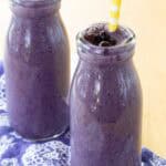 Two Blueberry Smoothies in glass bottles garnished with small thawed wild blueberries.