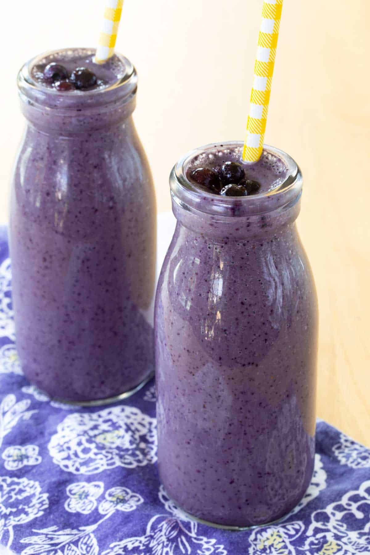 Two Blueberry Smoothies in glass bottles garnished with small thawed wild blueberries.