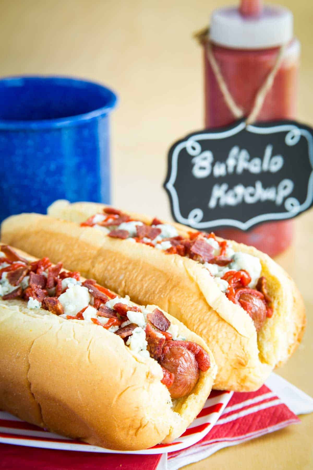 Grilled hot dogs in buns with bacon, blue cheese, and ketchup on top.