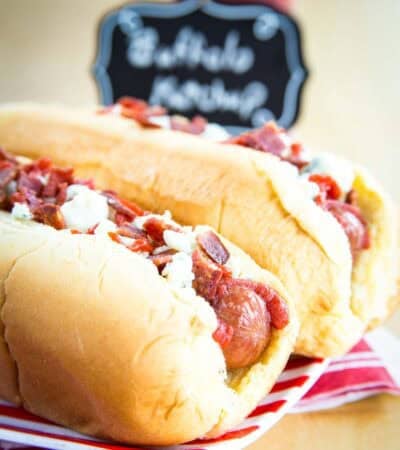 Closeup of a Buffalo Hot Dogs in a bun on a red and white striped plate.